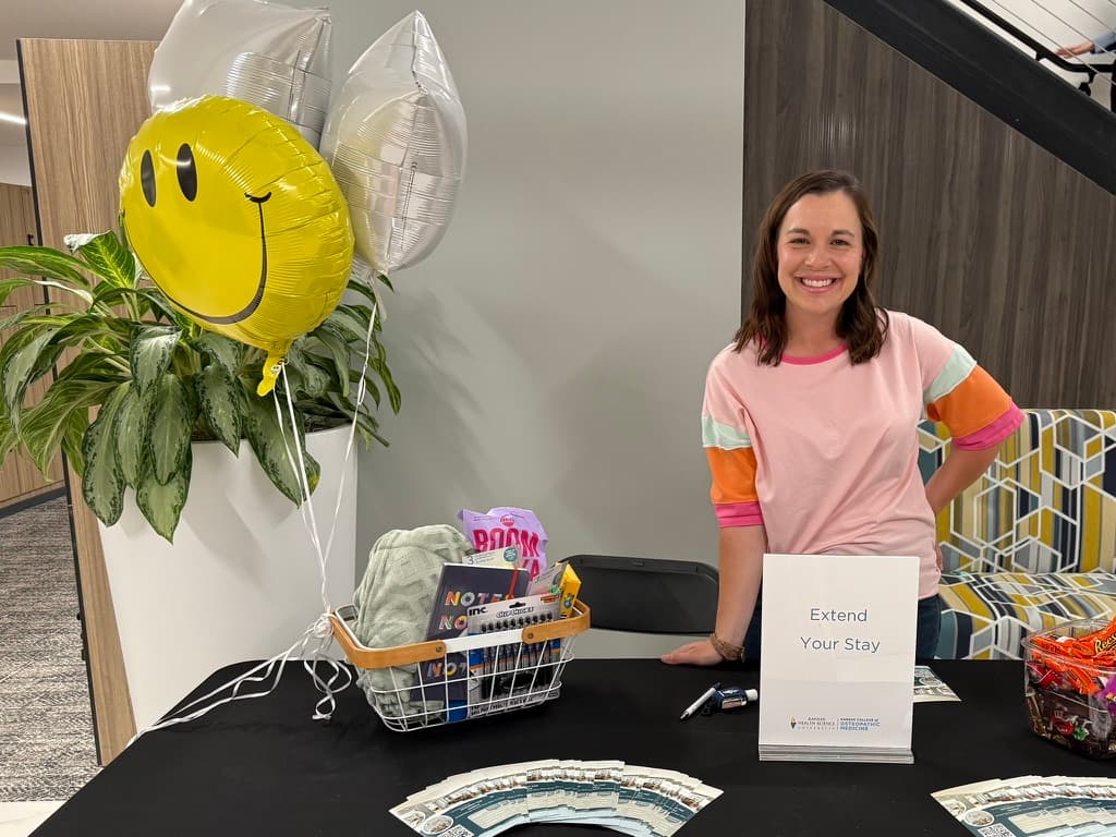 Emily smiling behind an Extend Your Stay table with a welcome basket and balloons